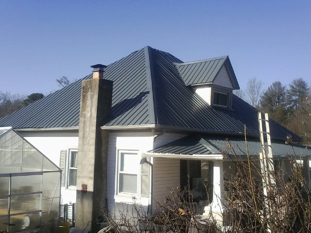 Dark blue standing seam metal roof on a white farmhouse with dormer — Slate & Tile Roof Repair by Roofing Brothers in Matagorda