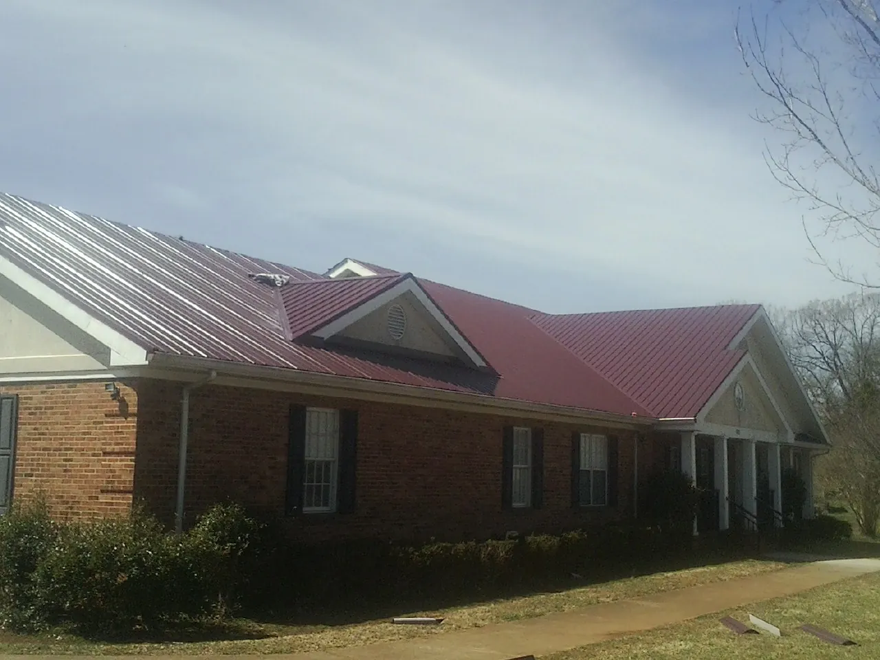 Red metal roof with gabled entries on a long brick building, from a Hail Damage Roof Repair job in Matagorda