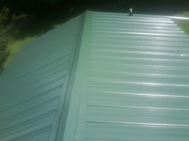 New green metal panels meeting at the ridge of a roof — Flat Roof Repair work by our crew in Matagorda
