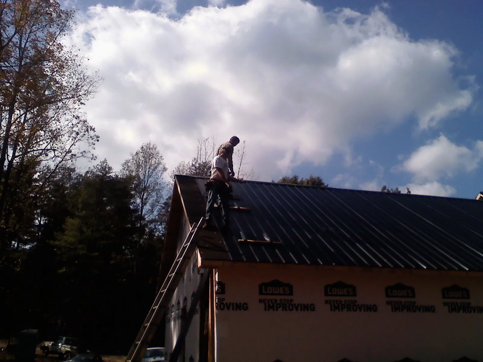Roofer fastening dark metal panels high against a cloudy sky, from a Roof Inspection job in Matagorda